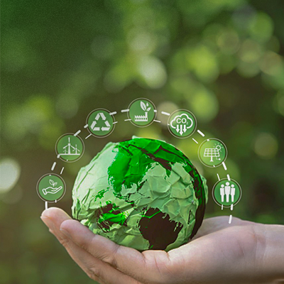 A hand holds a green paper globe surrounded by eco-friendly icons